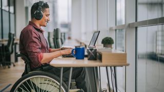 Man in wheelchair at desk with laptop and over-ear headphones