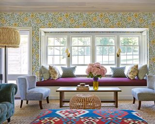 colorful living room with floral wallpaper, purple windowseat, blue sofa, patterned cushions and ikat footstool