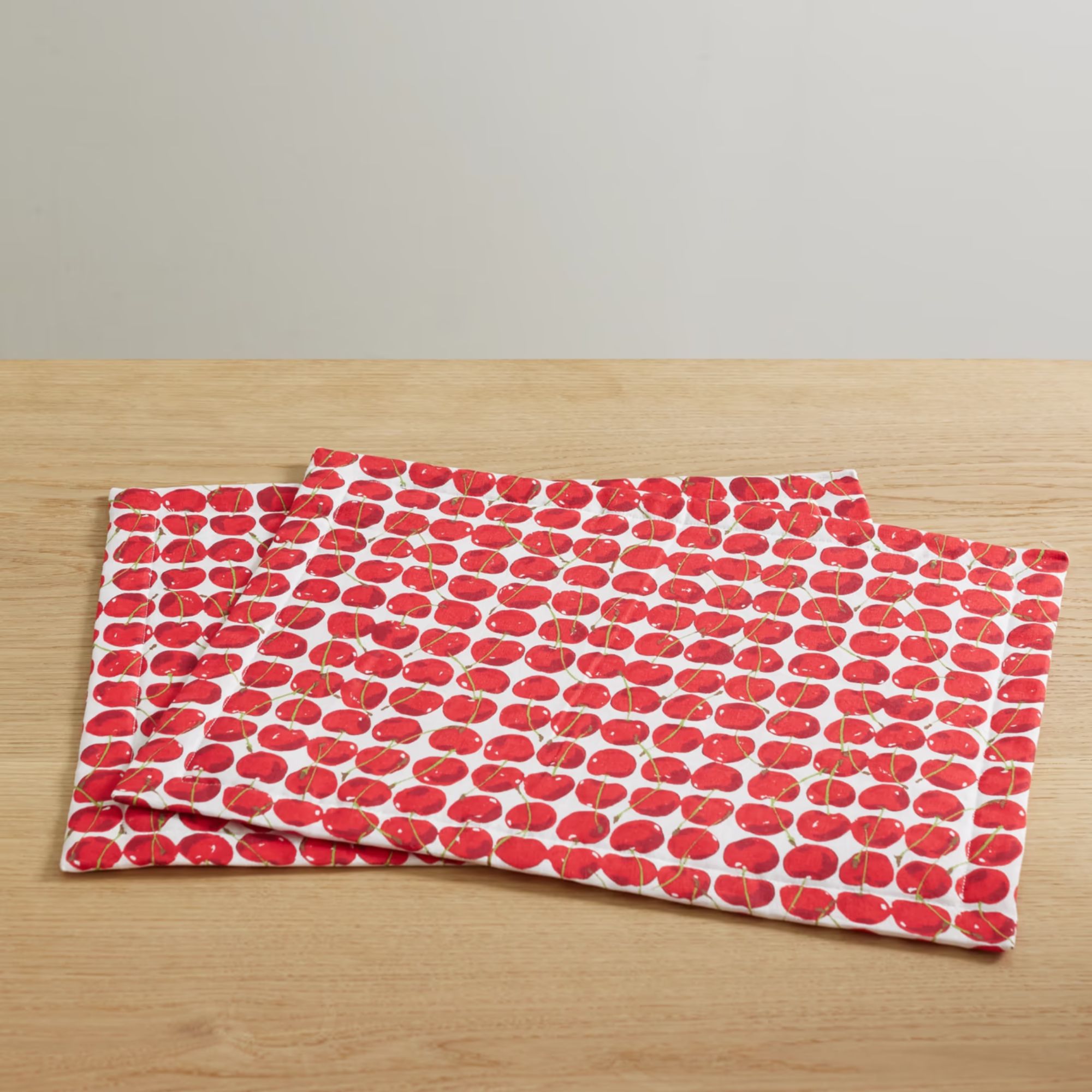 Two white linen placemats with a bright red cherry print