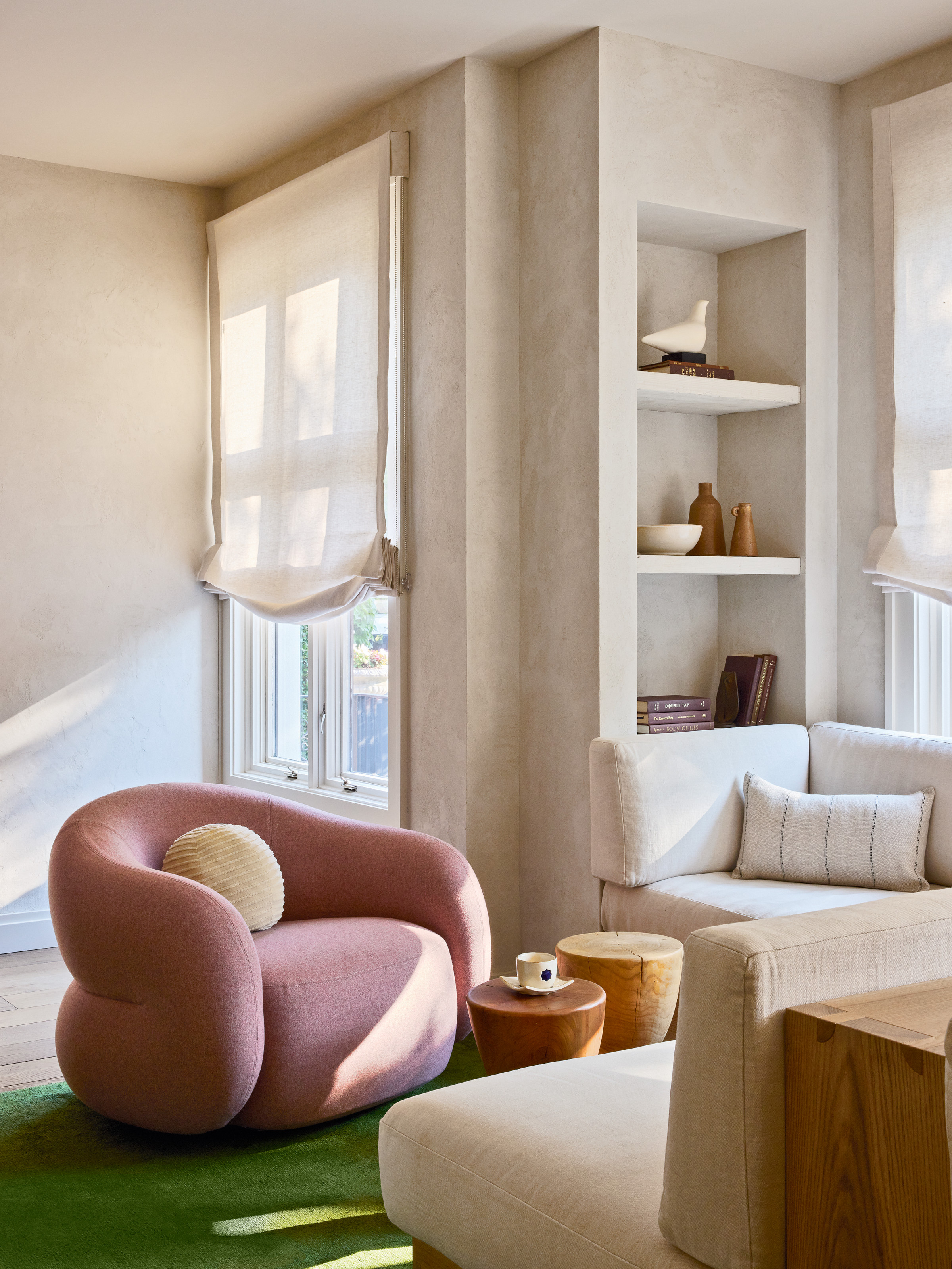 Lounge area with cream textured walls, pink armchair, green rug and cream corner sofa