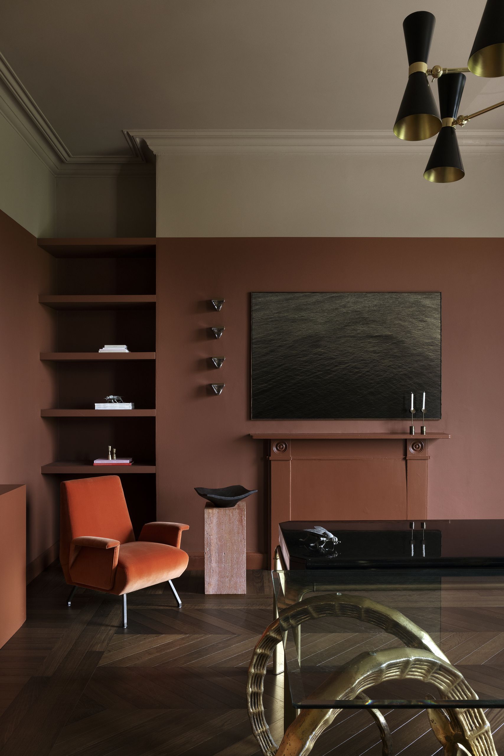 A modern living room with color-blocked walls in brick/burgundy red transitioning into a warm off-white. There is an orange accent chair.