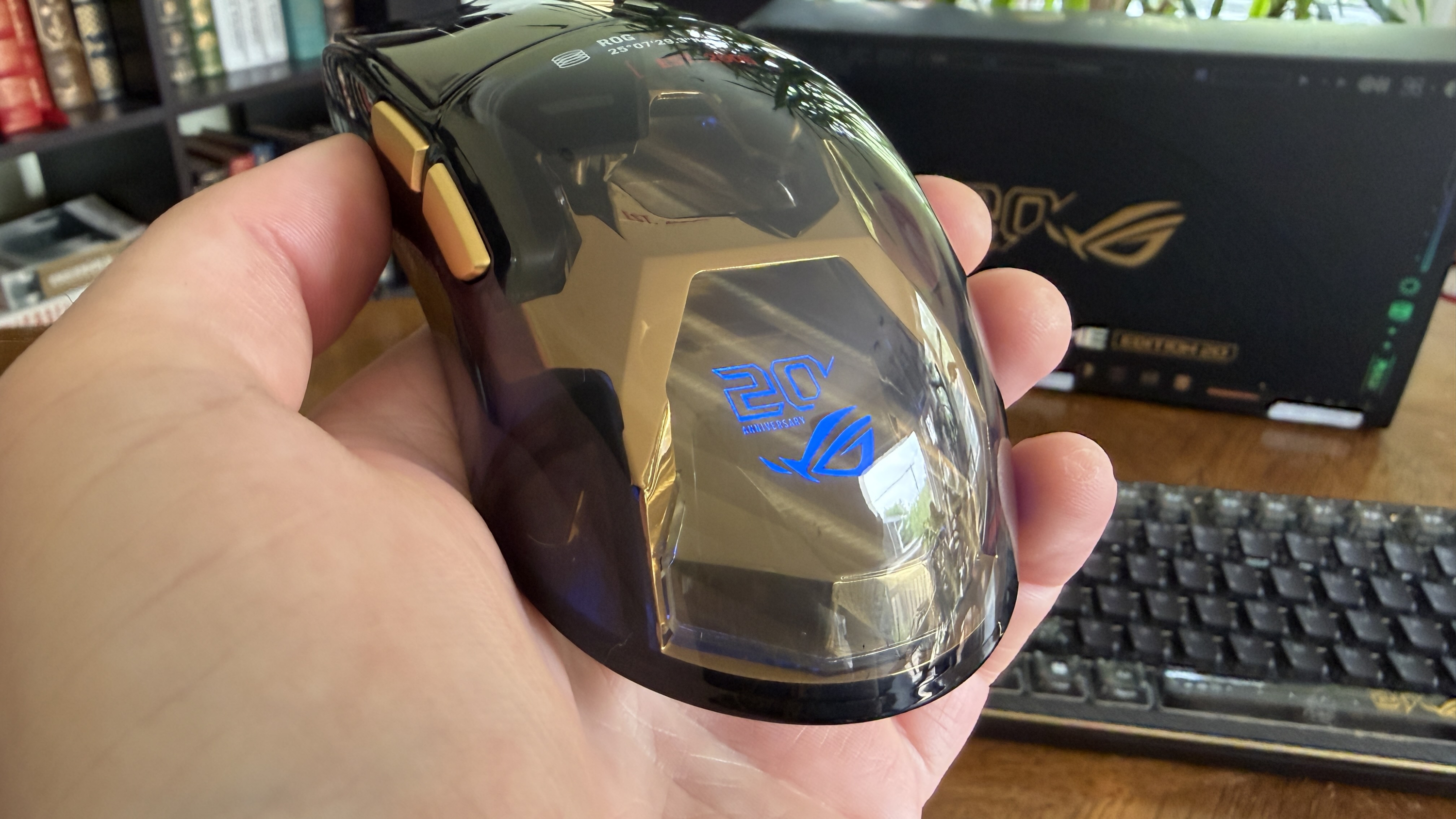 A 20th Anniversary edition ASUS ROG computer mouse with a reflective surface and golden accents.