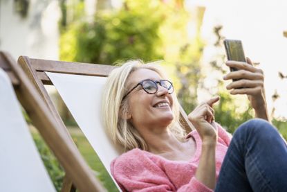 Smiling woman using smartphone while sitting on deckchair