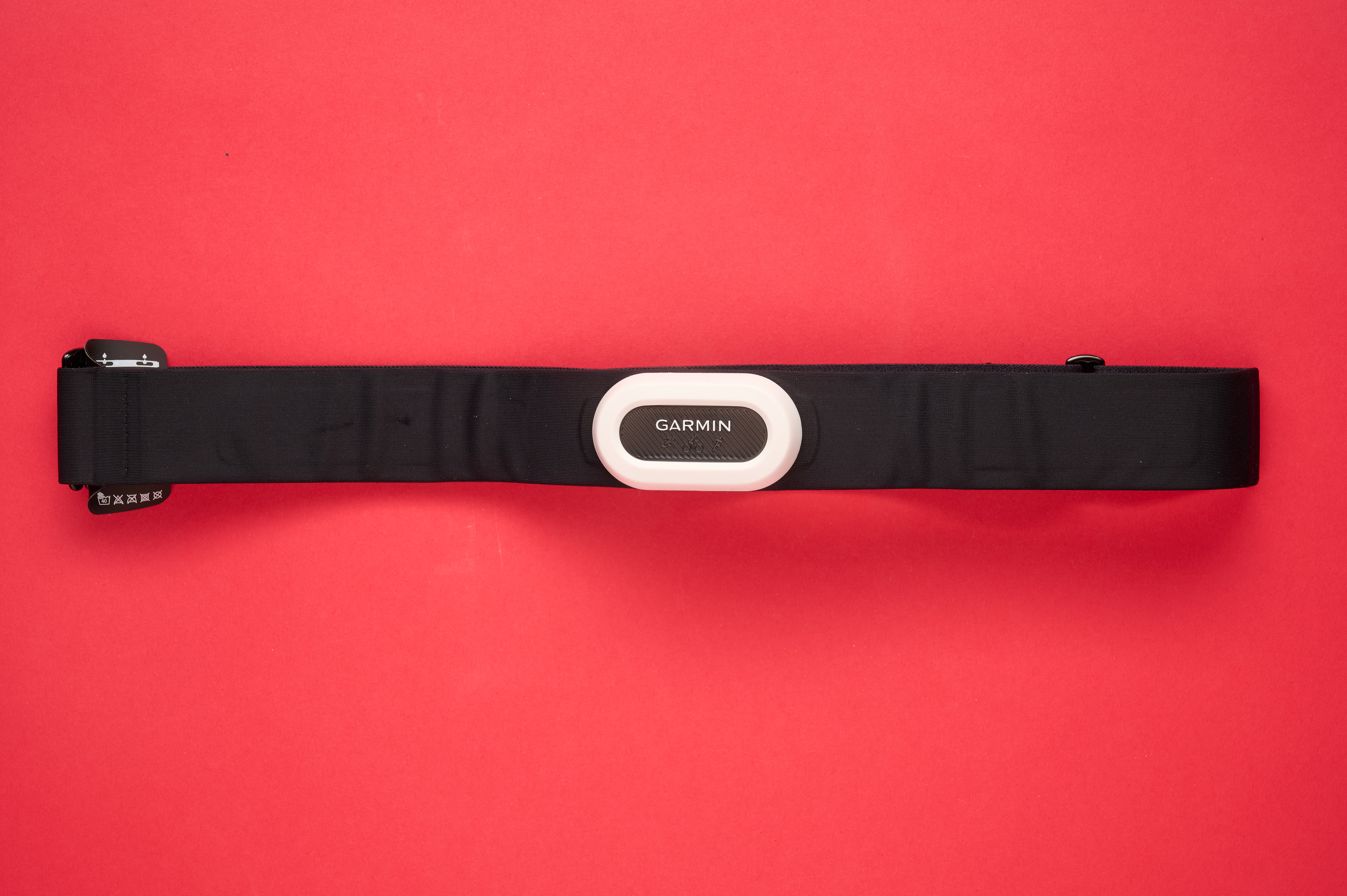 Garmin HRM-Pro Plus heart rate monitor with its pill like shaped body and white surround, laid flat on a red background