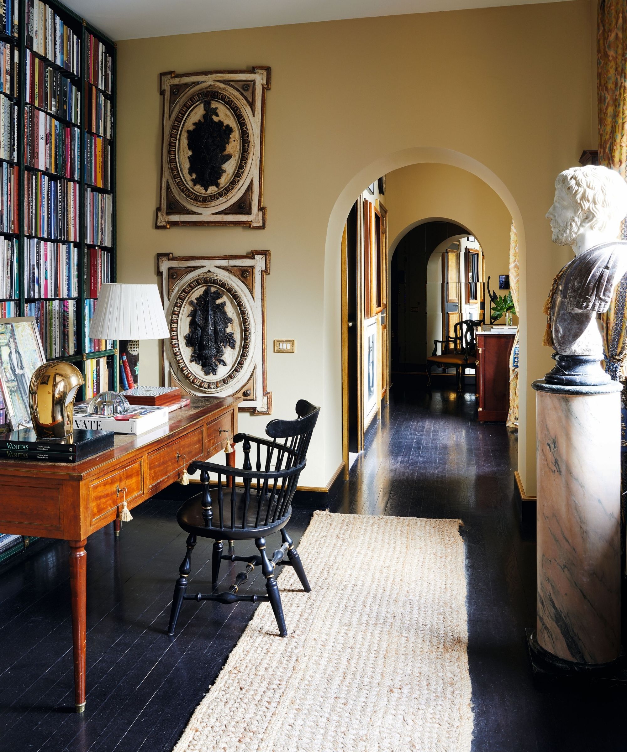 a warm yellow painted home office with a library wall and antique desk