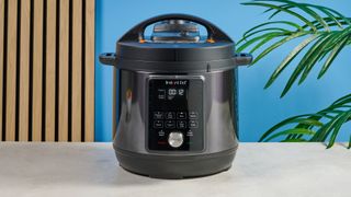 a black instant pot with a dial and touchpad is photographed against a blue background