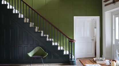 Hallway with rich green painted wall next to the stairs and navy painted panelling with wood floors