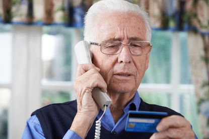 A man, who looks worried, talks on the telephone while looking at a credit card. 
