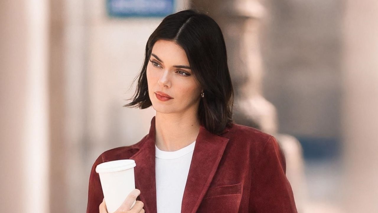 Kendall Jenner wears blue jeans, affordable loafers, red wine velvet jacket and a white tee as she carries a coffee cup