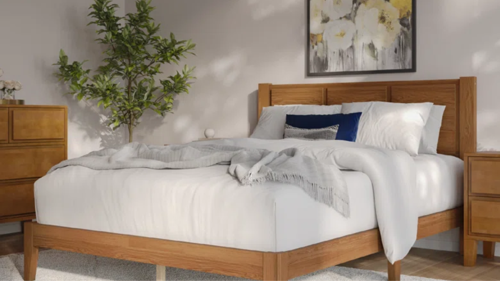 a bedroom with a light wood bedframe, white sheets and pillows, a light wood side table and dresser, and a large plant in the corner
