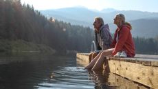 Mature couple relax on wooden pier, looks out across lake, BC, Canada.