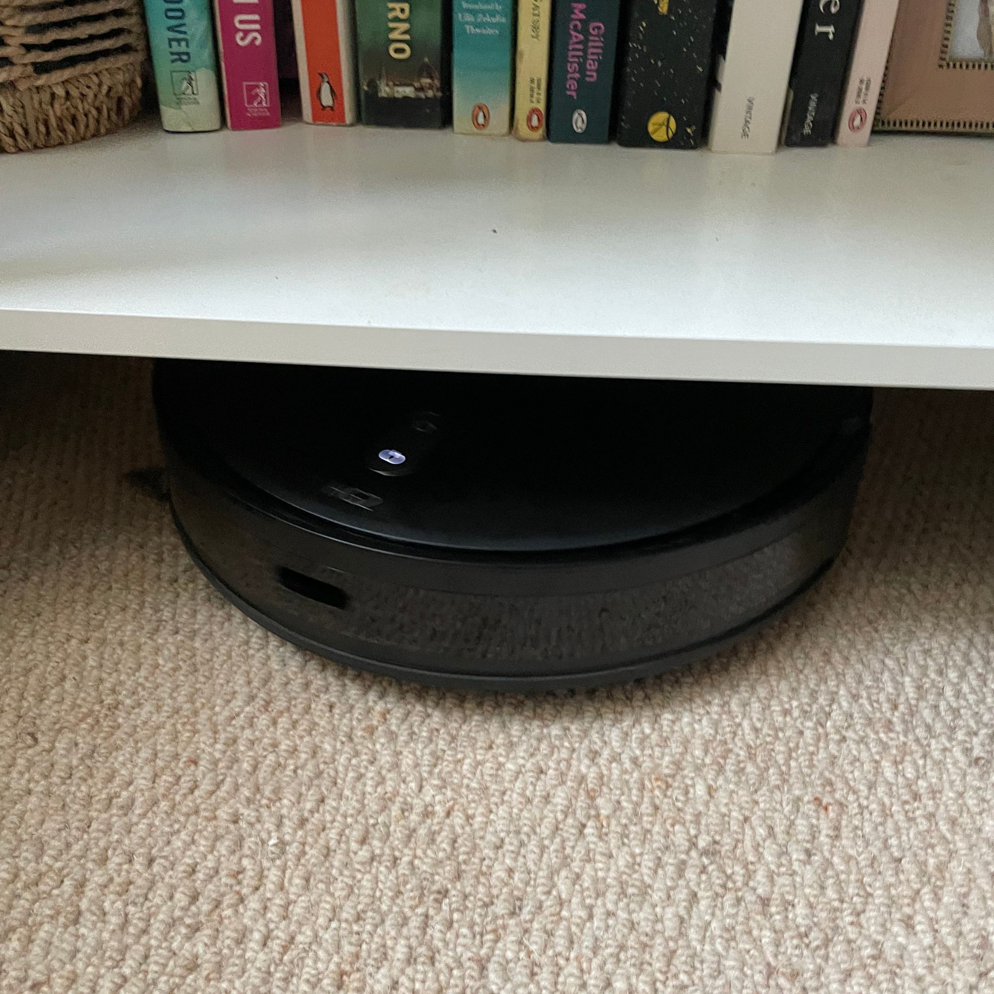 Hoover HG2 robot vacuum and mop underneath a low bookshelf