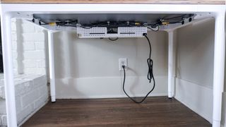 An under desk view of the Branch Four Leg Standing Desk and its optional cable organizer