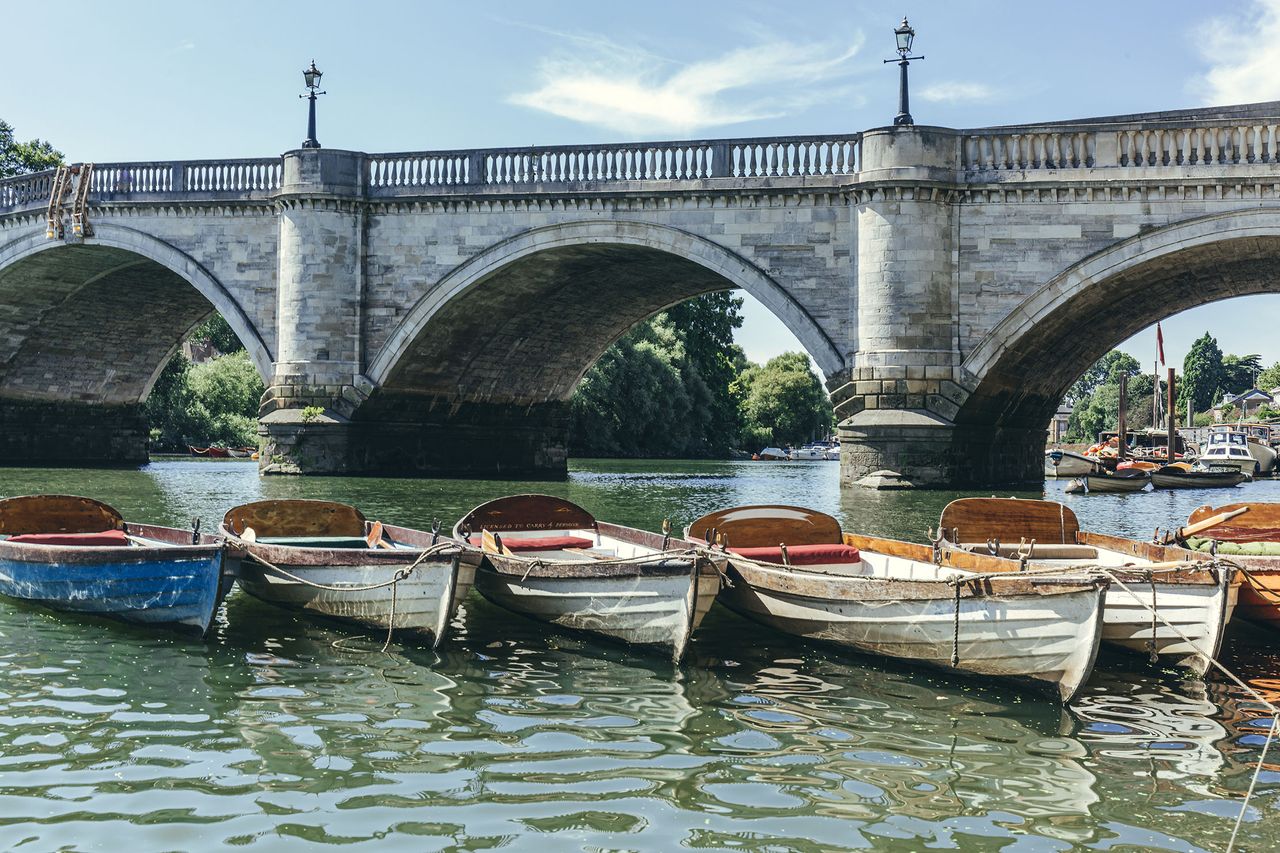 London&#039;s oldest bridge is also among its very prettiest. Wooden rowboats with oars inside, moored at the Thames riverside by Richmond Bridge.