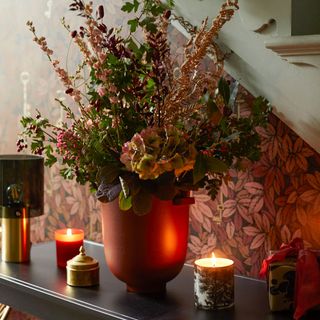 Floral wallpaper room with flowers in a vase on top of a wooden table next to burning candles