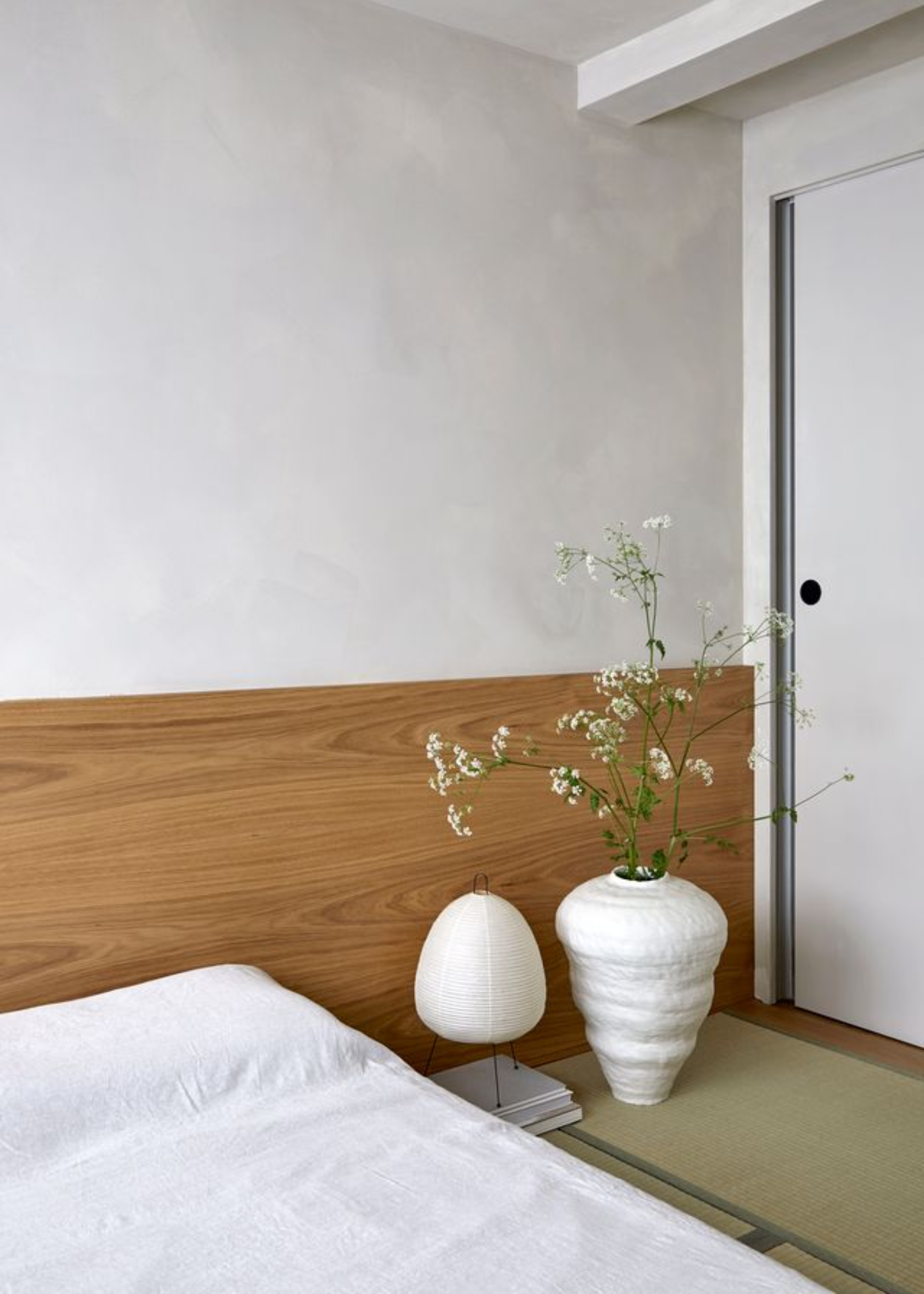 A floor mattress on a tatami mat beside a paper lamp and a white vase