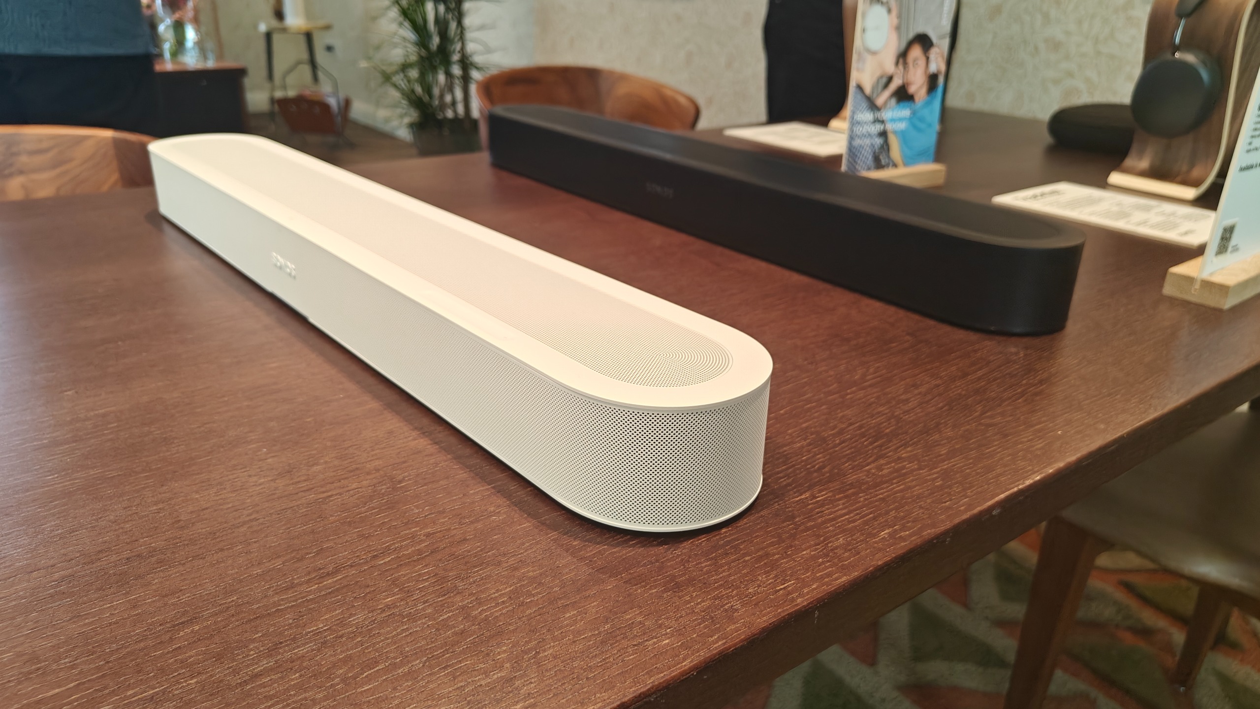Sonos Beam Ultra on a brown wooden table. Both the white and black editions are in view.