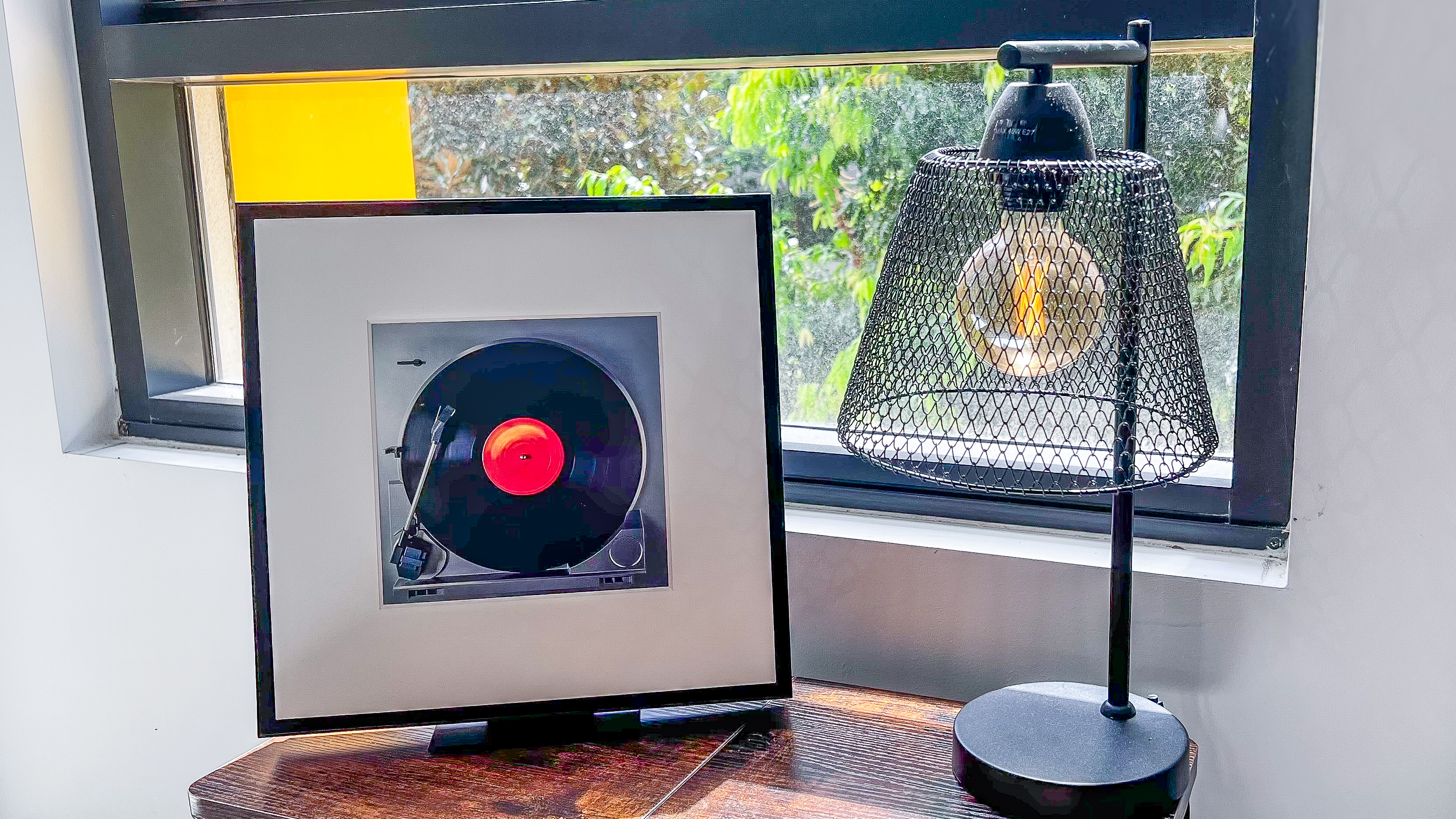 Samsung Music Frame and a lamp on a table in front of a window