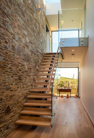 contemporary staircase in double height hallway with exposed stone wall