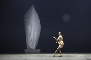 Woman dances in Issey Miyake dress beside large sculpture