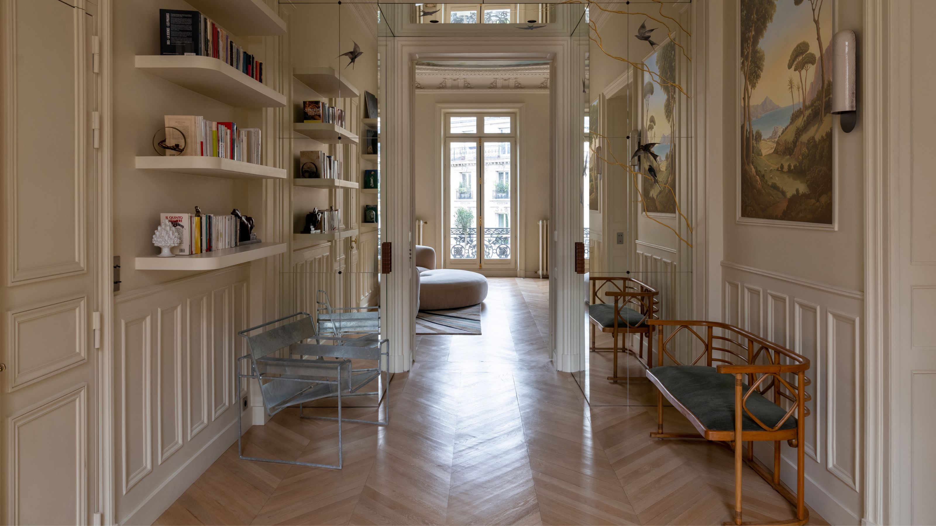 A grand hallway with off-white walls, paneling, and open shelving with seating benches along either side of the walls and paintings along the right-hand side
