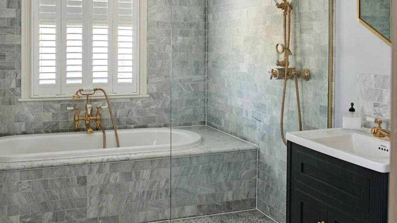 A gray bathroom with a tiled bath and a gold shower faucet
