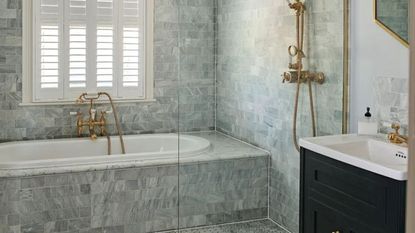 A gray bathroom with a tiled bath and a gold shower faucet