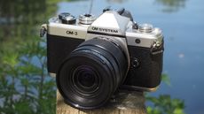 OM System OM-3 on a wooden post next to a pond