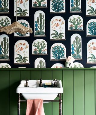 A traditional white sink in front of green wall panels and green botanical wallpaper