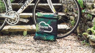 A bike cover in a square bag next to a bike wheel