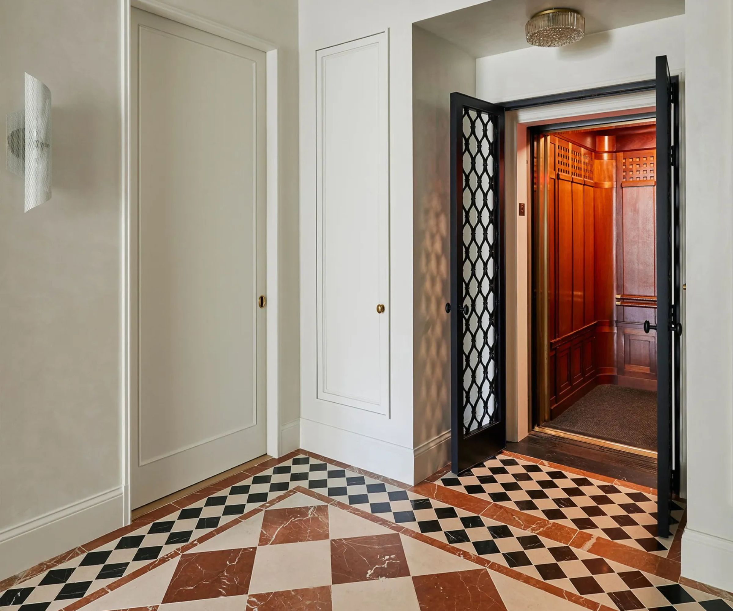White walled entryway with checkboards red, white and black marble tiles and a wooden clad lift