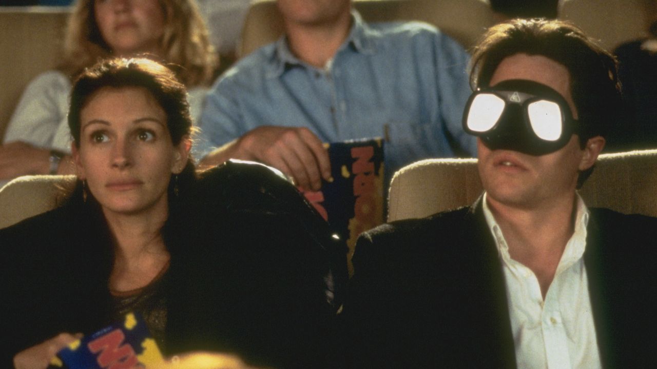 Julia Roberts and Hugh Grant sit in a movie theater in the movie Notting Hill, and Grant wears swimming goggles