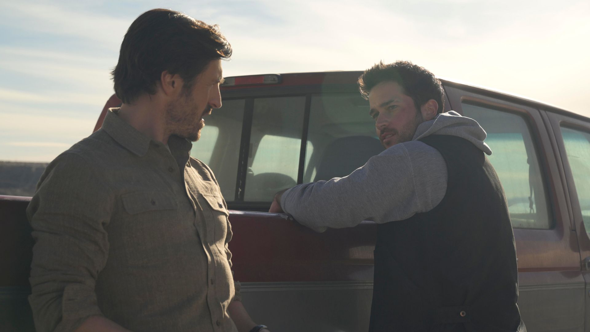 Yancy talks to a man while leaning forwards on a truck