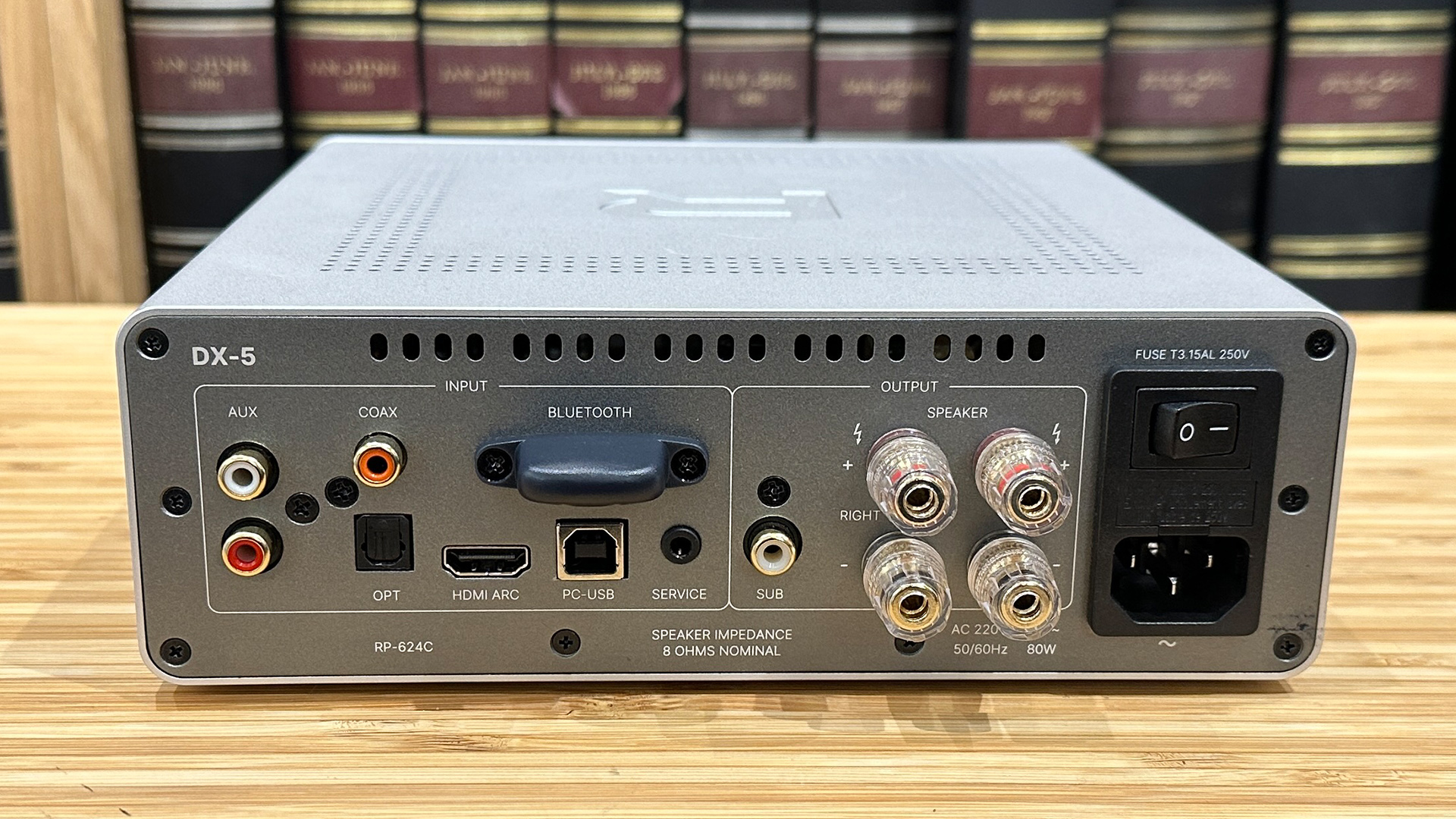 Rotel DX-5 integrated amplifier on wooden hi-fi rack in front of bookcase, back of unit showing connections