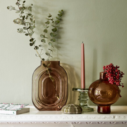 a sage green painted wall behind a selection of glass vases and candlesticks on a mantel piece