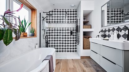 a bathroom with wood flooring, black and white patterned tiles, and marble tiled walls, with a pale grey twin vanity unit and storage baskets in a small alcove