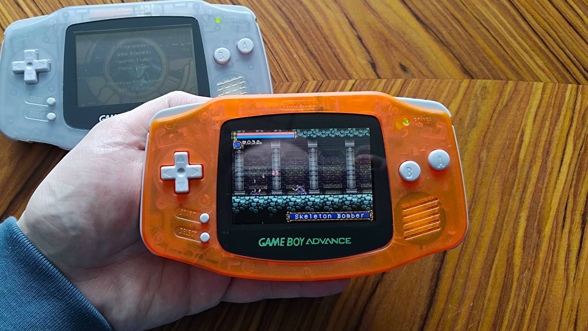 Orange GBA with backlit LCD screen and Castlevania gameplay with unmodded clear GBA in backdrop.