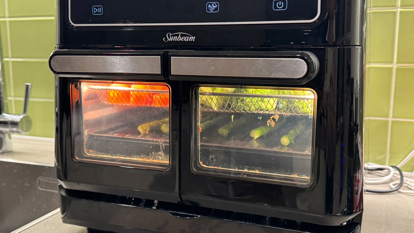 Two trays of vegetables inside the Sunbeam Multi Zone Air Fryer Oven with the doors closed and the internal light turned on