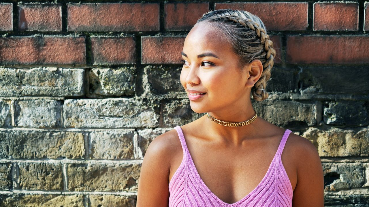 cute braided hairstyle a woman against a brick wall with a milkmaid braid, cute braided hairstyles