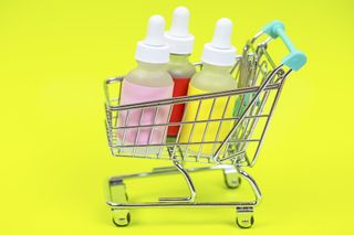 On a bright yellow background is a miniature shopping trolley. The trolley holds 3 small skincare bottles.