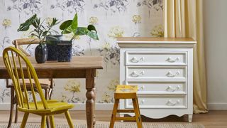 floral wallpaper behind drawers and wooden table