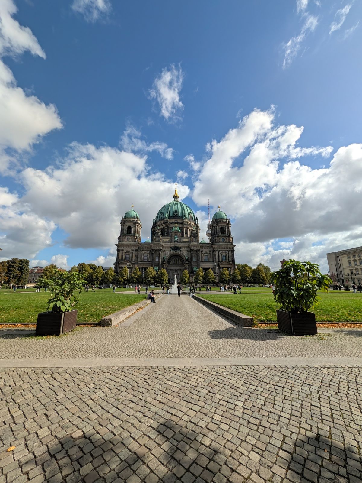 Wide-angle view of Berlin Cathedral across a landscaped lawn beneath a dramatic blue and cloudy sky.