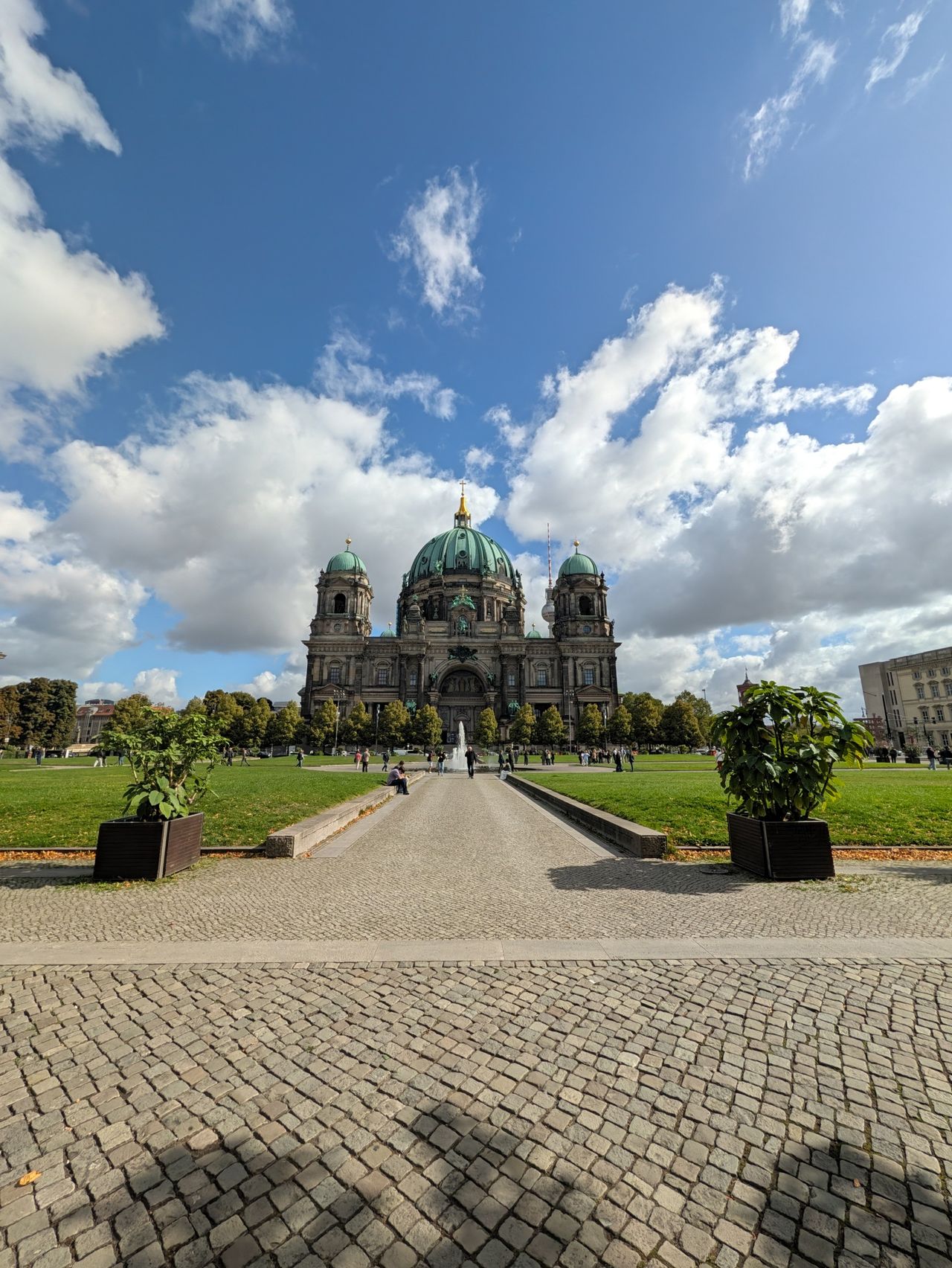 Wide-angle view of Berlin Cathedral across a landscaped lawn beneath a dramatic blue and cloudy sky.