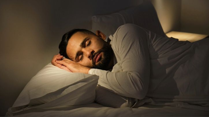 A man sleeping on his side in bed with white sheets and white night clothes