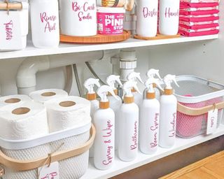 Under the sink kitchen storage with white bottles and pink labels