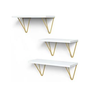 Three white floating shelves with gold triangle brackets