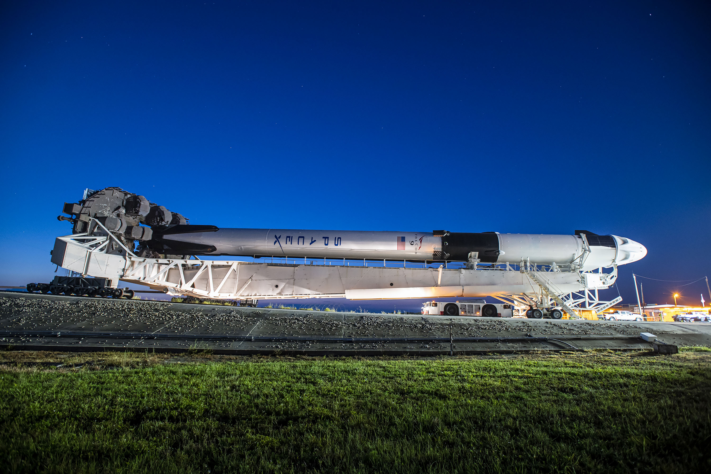 rocket lying on its side on a crawler with grass below and the rising sun behind