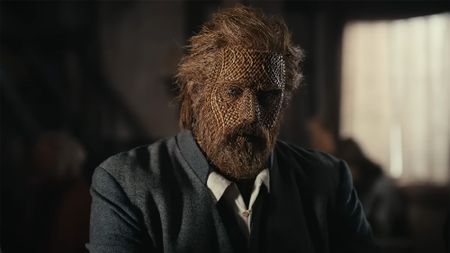Alexander Skarsgard in a suit and full Wicker face makeup and coverings playing the wooden lover. 