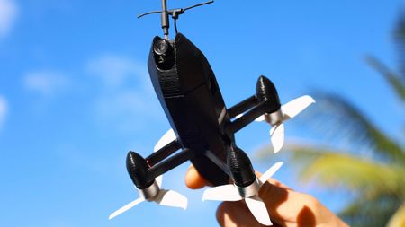 The ESP32 self build rocket drone being held up, with a blue sky and palm tree backdrop