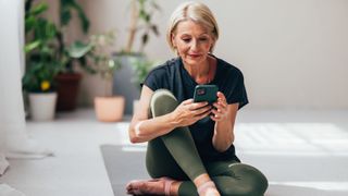 Woman looking at phone sitting on a yoga mat